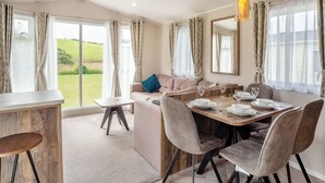 A dining area with a table set for four, a sofa, and a view of the outdoors. - 12ft-wide luxury caravan with one double and two twin. (Charmouth)