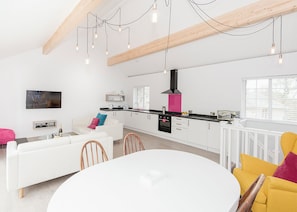 Una cocina moderna con armarios blancos, una campana extractora negra y un comedor con mesa y sillas blancas.