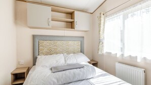 Une chambre à coucher comprenant un lit, une tête de lit à motifs chevrons, une table de chevet, une armoire et une fenêtre avec des rideaux.