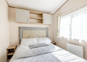 Un dormitorio con cama, cabecera estampada en patrón de grecas, mesita de noche, armario y ventana con cortinas.