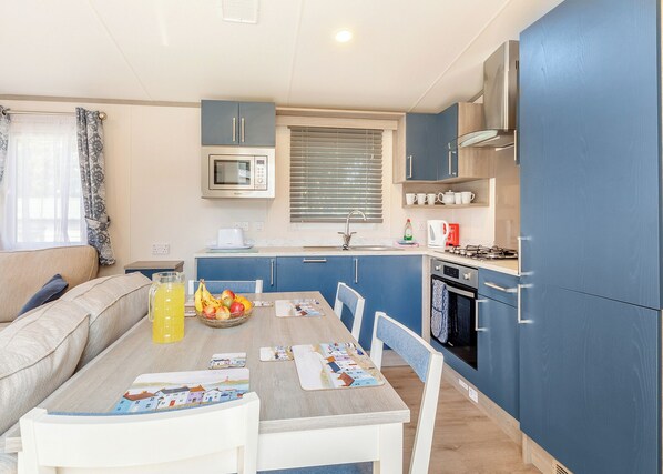 A compact kitchen with a microwave, stove, and sink. There's a dining table with chairs and a bowl of fruit.