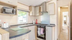 Une cuisine compacte équipée d’un four à micro-ondes, d’une cuisinière et d’un four, une fenêtre avec vue et une porte donnant sur une autre pièce.