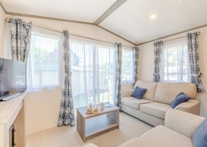 A living room with a sofa, a coffee table, a TV, and large windows with curtains.