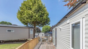 Une maison mobile dotée d’une terrasse, d’une table avec des chaises et d’un grand arbre.