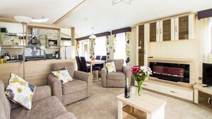 A modern living room with sofas, a dining table, a fireplace, and a TV. - Oak 3 Hot Tub + Private Garden (Axminster)
