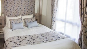 A hotel room with a bed, floral-patterned headboard, and curtains. - Oak 3 Hot Tub + Private Garden (Axminster)