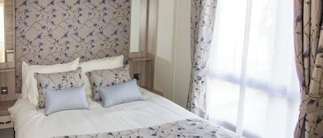 Quarto de hotel com cama, cabeceira estampada com flores e cortinas.