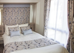 A hotel room with a bed, floral-patterned headboard, and curtains. - Oak 3 Hot Tub + Private Garden (Axminster)
