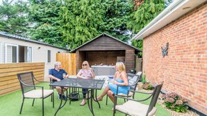 A patio with a table and chairs, a wooden fence, and a brick wall with a decorative element. - Oak 3 Hot Tub + Private Garden (Axminster)