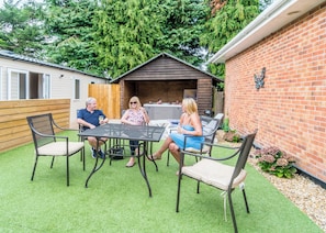 A patio with a table and chairs, a wooden fence, and a brick wall with a decorative element. - Oak 3 Hot Tub + Private Garden (Axminster)