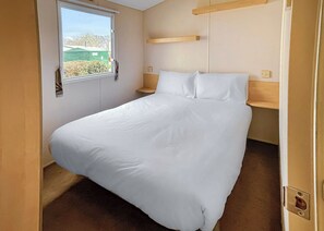 Una habitación pequeña con cama individual, ventana, mesita de noche y estante en la pared.