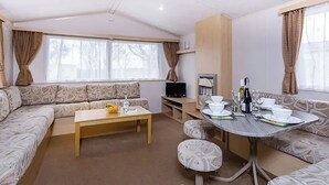 A living room with a sofa, a coffee table, a TV, and a dining table set for two. - 3 bedroom accommodation in Newbridge, Nr Yarmouth (Newbridge, Nr Yarmouth)