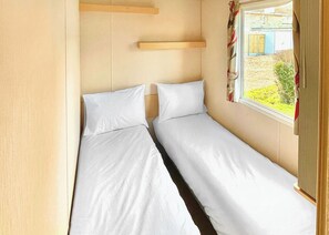 Habitación pequeña con dos camas, una ventana con cortinas y un estante de madera.