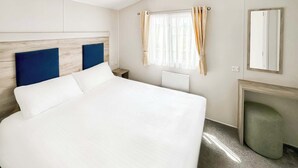 Una habitación de hotel con una cama grande, un cabecero de madera, una ventana con cortinas, un espejo y un radiador.