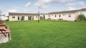 A two-story building with a flat roof, a grassy yard, and picnic tables. - Bungalow with one double and one twin. (Trearddur Bay, Holyhead)