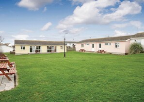 A two-story building with a flat roof, a grassy yard, and picnic tables. - Bungalow with one double and one twin. (Trearddur Bay, Holyhead)