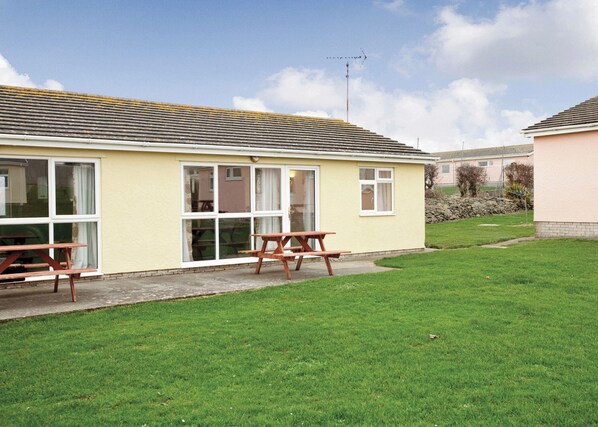 A yellow building with large windows and a picnic table in the yard.