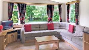 Un salon confortable avec un canapé, une table basse, un téléviseur et des rideaux.