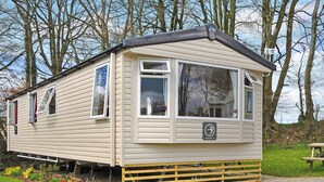 A mobile home with a small porch, a window with a 'SWIFT' sign, and a grassy area with a picnic table. - Luxury modern and spacious 12ft-wide caravan with one double and two twin. (Tavistock)