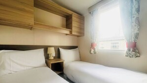 Une chambre avec deux lits, une table de chevet, une lampe et une fenêtre avec des rideaux.