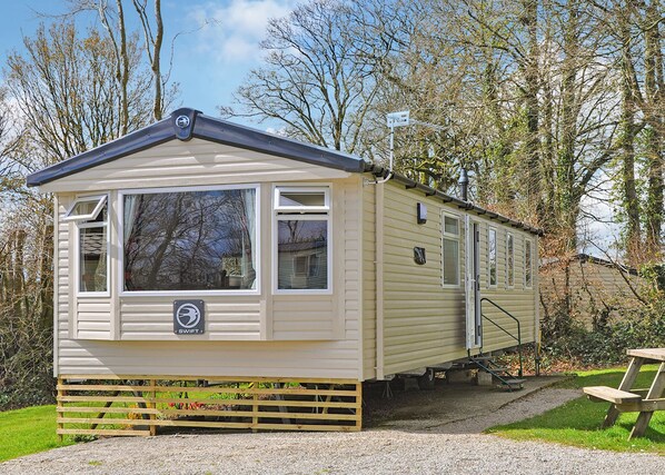 Une maison mobile dotée d’un porche à l’avant, d’une petite dépendance attenante et d’une table de pique-nique.