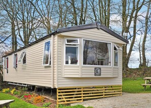 A mobile home with a small porch, a window with a 'SWIFT' sign, and a grassy area with a picnic table. - Luxury modern and spacious 12ft-wide caravan with one double and two twin. (Tavistock)