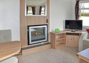 A compact RV interior with a wood-paneled wall, a fireplace, a television, and a small seating area. - Luxury modern and spacious 12ft-wide caravan with one double and two twin. (Tavistock)