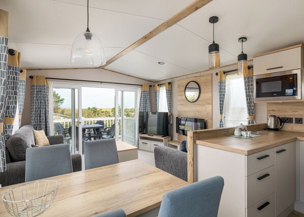 A modern RV kitchen with a dining area, large windows, and a view of the outdoors.