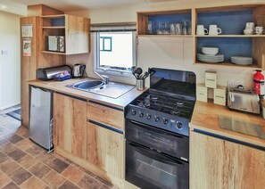 A compact kitchen with a built-in stove, oven, and sink, wooden cabinets, and a window. - Well presented 12ft-wide caravan with one double and one twin. (Clunderwen, Nr Narberth)