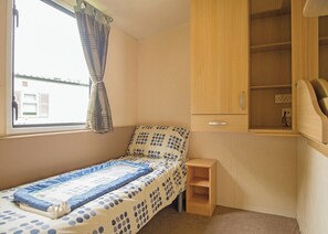 A small, single-bed room with a window, a wooden cabinet, and a small shelf. - Well presented 12ft-wide caravan with one double and one twin. (Clunderwen, Nr Narberth)