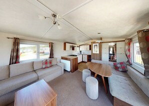 A compact RV interior with a kitchenette, a dining area, and a seating area with a sofa and ottomans. - Well presented 12ft-wide caravan with one double and one twin. (Clunderwen, Nr Narberth)