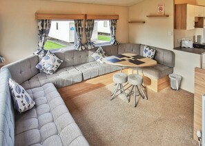 A caravan interior with a sofa set, a round table, and a kitchen area. - Well presented 12ft-wide caravan with one double and one twin. (Clunderwen, Nr Narberth)