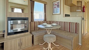 A compact kitchenette with a built-in oven, a seating area with a round table, and a window with curtains. - Comfortable caravan with one double and one twin. (Ingoldmells, Nr Skegness)