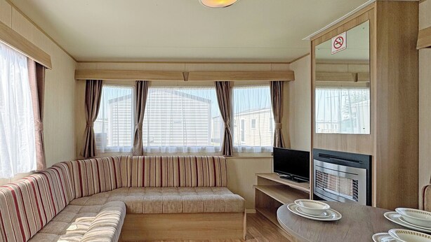 A compact living space with a sofa, a television, a dining table with plates, and a no-smoking sign. - Comfortable caravan with one double and one twin. (Ingoldmells, Nr Skegness)