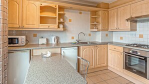A compact kitchen with wooden cabinets, a microwave, a toaster, a kettle, a sink, and a stove. - 1 bedroom accommodation in Silloth (Silloth)