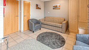 A room with a wooden door, a grey armchair, a beige sofa, a round grey rug, and a wardrobe. - 1 bedroom accommodation in Silloth (Silloth)