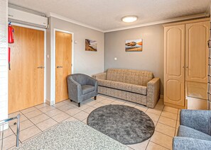 A room with a wooden door, a grey armchair, a beige sofa, a round grey rug, and a wardrobe. - 1 bedroom accommodation in Silloth (Silloth)