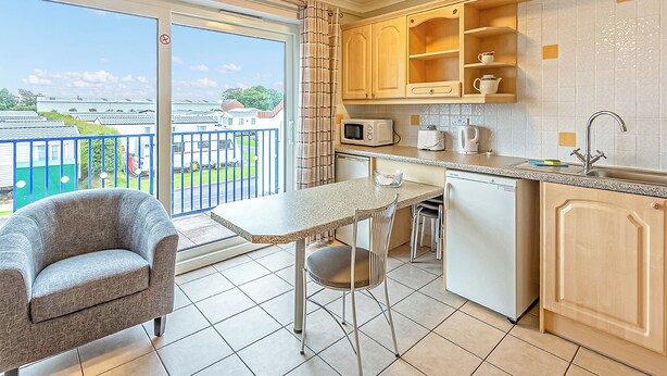 A balcony with a view of a residential area, a kitchenette with a microwave, toaster, and sink, and a chair. - 1 bedroom accommodation in Silloth (Silloth)