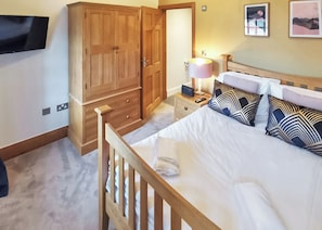 A bedroom with a wooden bed, bedside tables, a lamp, and a TV mounted on the wall. - Carmarthenshire Cottage (Clunderwen, Nr Narberth)