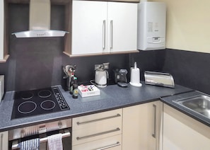 A compact kitchen with a stove, a coffee maker, a toaster, and a box labeled 'CLIPPER'. - Carmarthenshire Cottage (Clunderwen, Nr Narberth)