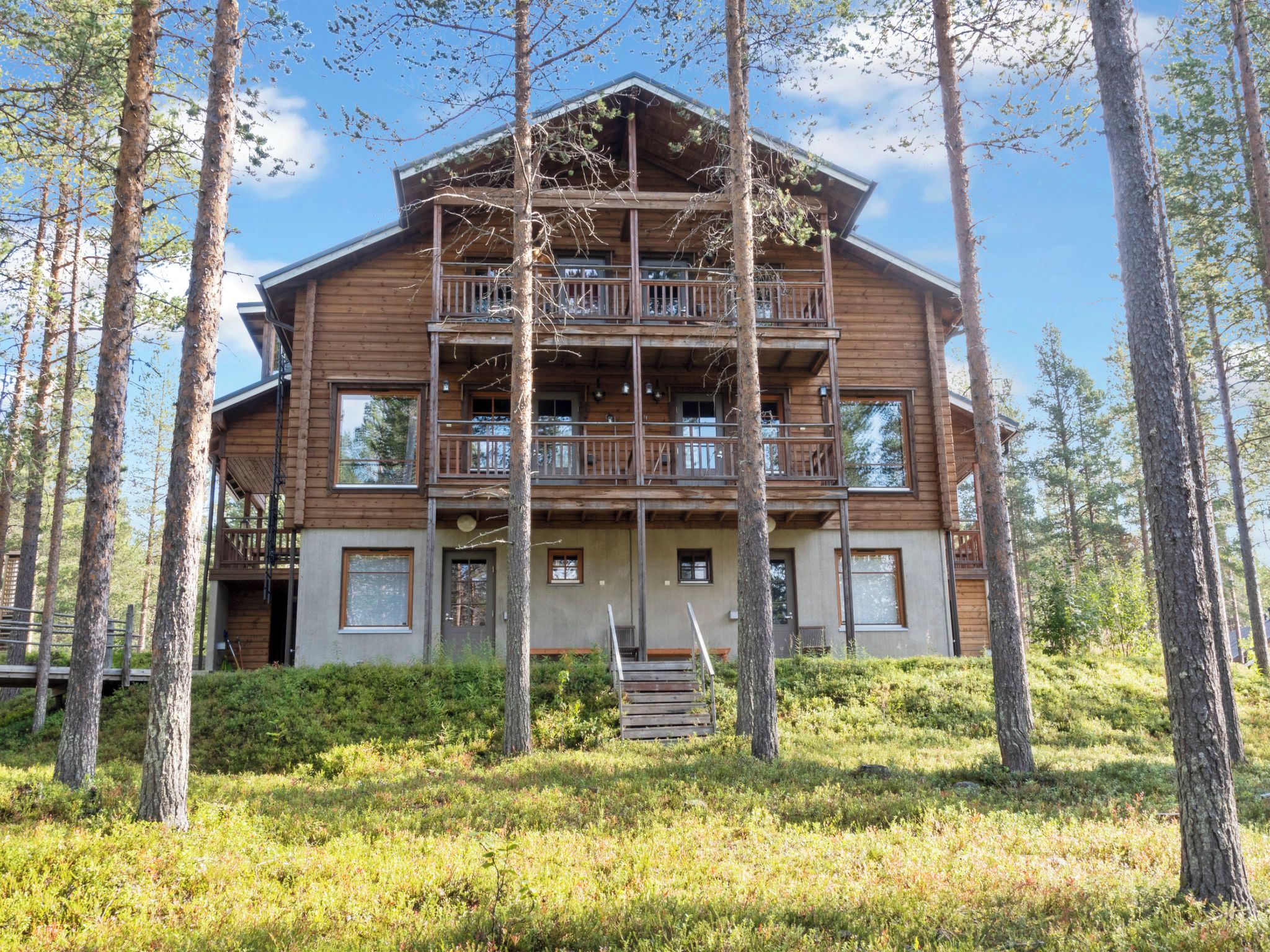 Een houten vakantiehuis met meerdere verdiepingen en balkons, omgeven door bomen en een gazon.
