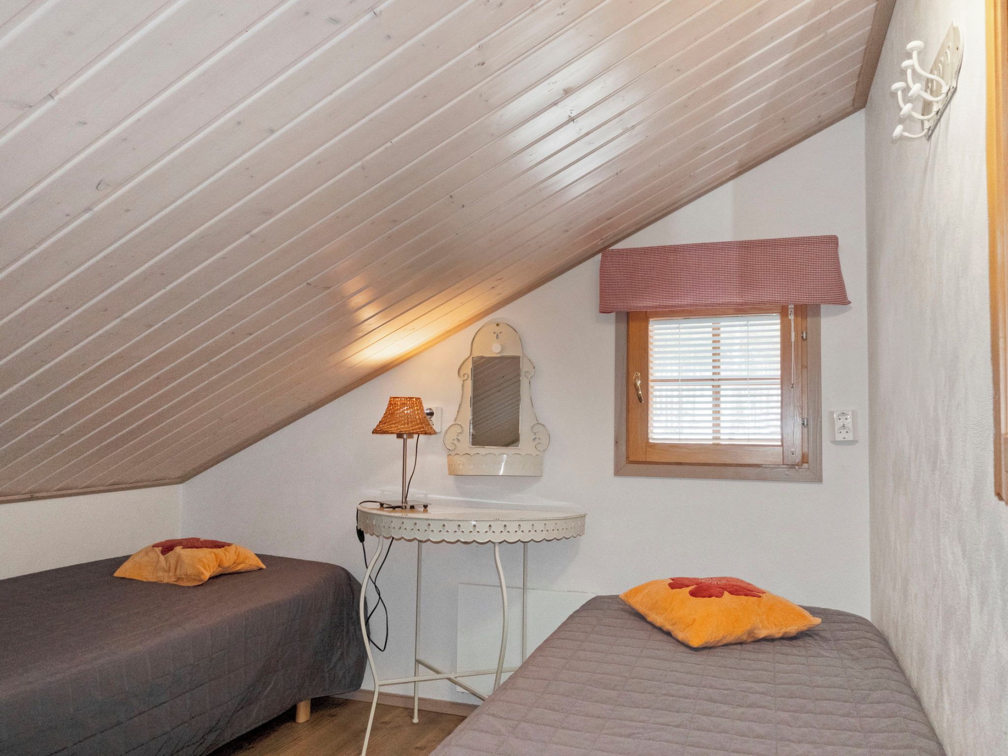 Een knus, compacte kamer met twee bedden, een nachtkastje, een spiegel en een raam met jaloezieën.