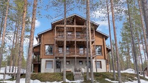 Une cabane en bois à plusieurs étages, dotée de balcons, entourée de grands arbres et d’un sol recouvert de neige.