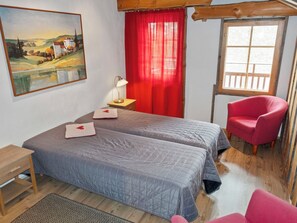 A bedroom with two beds, a red chair, a wooden desk, a lamp, and a painting on the wall. - Nuovo casa b by Interhome (Kittilä)