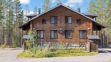 A wooden cabin with a sign indicating it is a new house, surrounded by a forest.