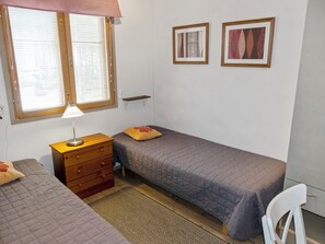 Une chambre avec deux lits, une table de chevet, une lampe, une chaise et deux tableaux encadrés au mur.