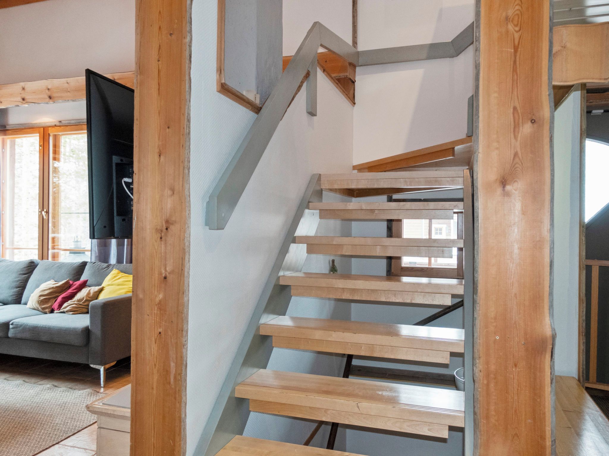 A modern interior with a wooden staircase, a grey sofa, and a flat-screen TV.