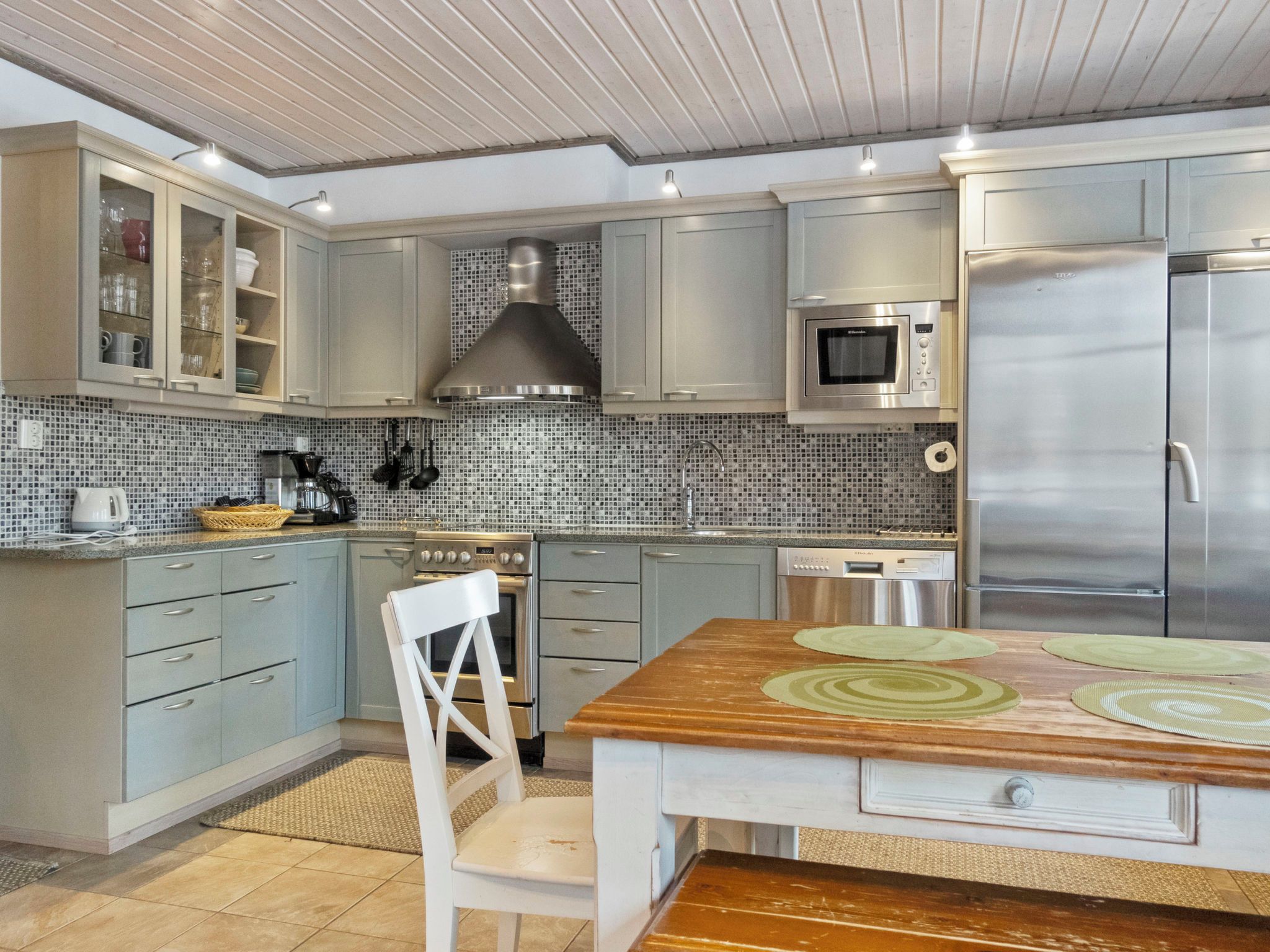 A modern kitchen with grey cabinets, a stainless steel range hood, a microwave, and a refrigerator.