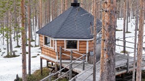 Une cabane en bois avec un toit noir, entourée d’arbres et de neige.