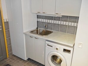 Une cuisine compacte équipée d’un lave-linge intégré, d’un évier et d’un crédence carrelée.